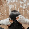 Yura Knit Fingerless Alpaca Gloves Awamaki Peru White - lifestyle image of woman standing with her back towards the camera against a brown clay wall wearing winter gloves